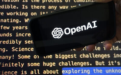 The OpenAI logo appears on a mobile phone in front of a screen showing a portion of the company website in New York, November 21, 2023. (Peter Morgan/AP)