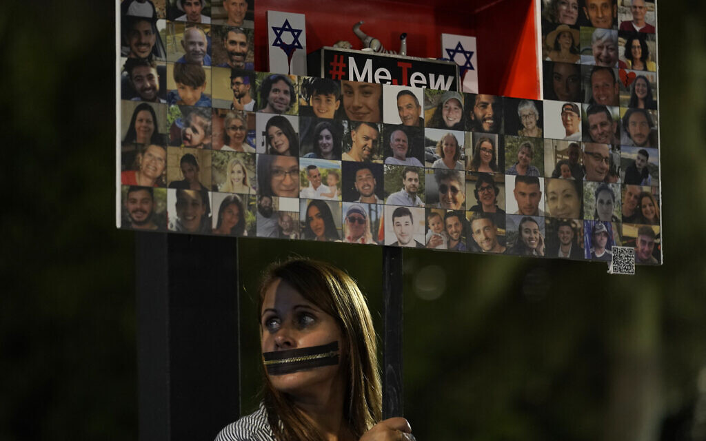 An Israeli holds a placard with pictures of hostages held in the Gaza Strip, in a show of solidarity, in Tel Aviv, November 25, 2023. (AP Photo/ Leo Correa)