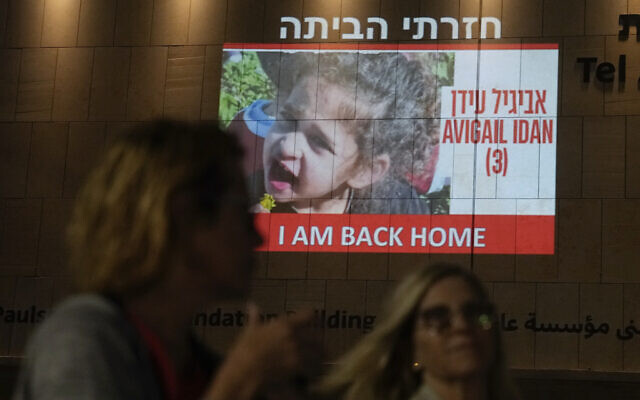 People walk past an image of 4-year-old Avigail Idan, a hostage held by Hamas who was released on Sunday, projected onto a building in Tel Aviv, November 26, 2023. (AP Photo/Ariel Schalit)