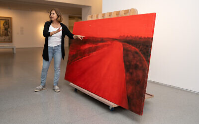 Artist Ziva Jelin with her painting, 'Curving Road,' damaged in the October 7, 2023, attack by Hamas terrorists at Kibbutz Be'eri, before it is temporarily hung in the Israel Museum, November 2023 (Courtesy Zohar Shemesh)