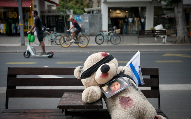 A blindfolded large teddy bear with fake blood on it, along with a photograph of an Israeli child held hostage by Hamas terrorists in Gaza since the October 7 massacre, as part of an exhibit in Tel Aviv, November 13, 2023. (Miriam Alster/FLASH90)
