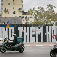 People pass a mural in Florentine, southern Tel Aviv, calling for the release of the Israeli hostages held by Hamas in Gaza. November 28, 2023. (Miriam Alster/FLASH90)