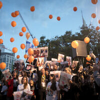 Israelis hold photographs of the Bibas family, and orange balloons to represent the redheaded children, at a press conference calling for the release of 10-month-old Kfir, 4-year-old Ariel, and their parents Shiri and Yarden Bibas, at  'Hostage Square' in Tel Aviv, November 28, 2023 (Miriam Alster/Flash90)