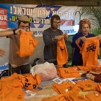 Activists fold T-shirts printed with the message 'Returning Home.' Orange was the symbol of the struggle against the 2005 Gaza disengagement plan. Ashdod, November 22, 2023. (Mati Wagner/Times of Israel)