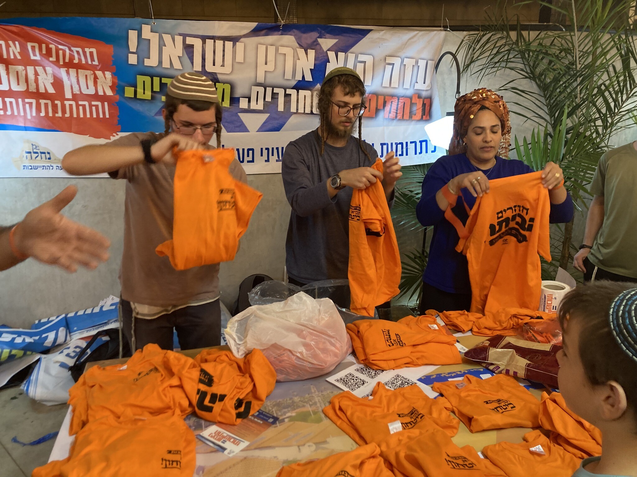 Activists fold T-shirts printed with the message 'Returning Home.' Orange was the symbol of the struggle against the 2005 Gaza disengagement plan. Ashdod, November 22, 2023. (Mati Wagner/Times of Israel)
