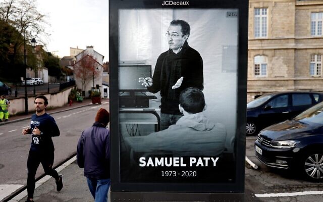 Pedestrians pass by a poster depicting French teacher Samuel Paty placed in the city center of Conflans-Sainte-Honorine, 30kms northwest of Paris, on November 3, 2020, following the beheading of the teacher on October 16. (Thomas Coex/AFP)