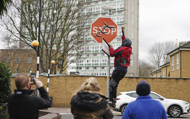 A person removes a piece of art work by Banksy, which shows what looks like three drones on a traffic stop sign, which was unveiled at the intersection of Southampton Way and Commercial Way in Peckham, south east London, Dec. 22, 2023. (Aaron Chown/PA via AP)