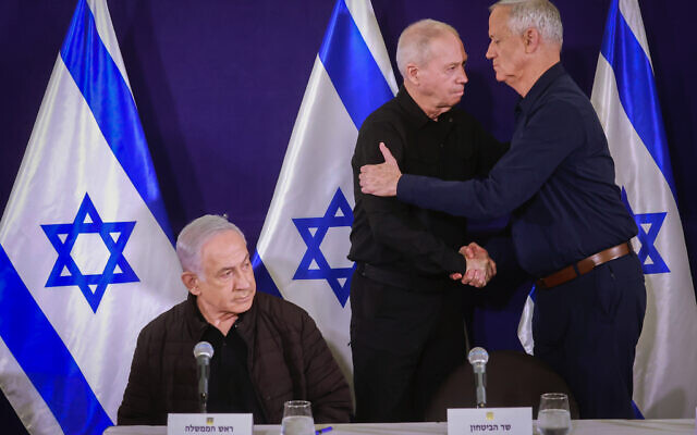 Defense Minister Yoav Gallant (center) and Minister Benny Gantz (right) embrace, with Prime Minister Benjamin Netanyahu at left, at a joint press conference at the Defense Ministry in Tel Aviv on November 11, 2023. (Marc Israel Sellem/POOL)