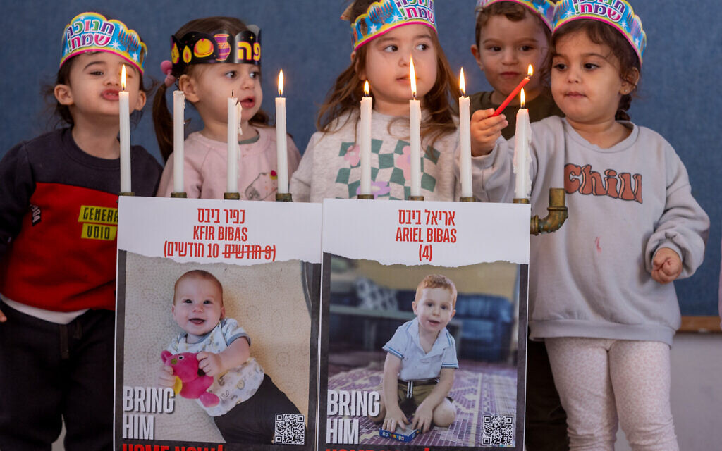 Photographs of Kfir and Ariel Bibas, who are held hostage by Hamas terrorists in Gaza, seen on a menorah being lit by children at a kindergarden in Moshav Yashresh, central Israel, during Hanukkah, on December 12, 2023. (Yossi Aloni/Flash90)