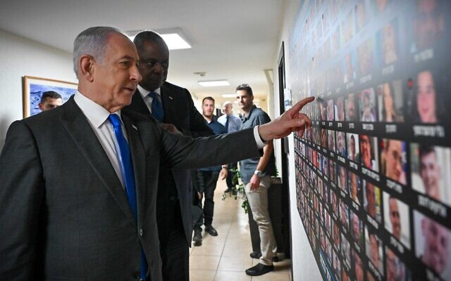 In this government handout photo, Prime Minister Benjamin Netanyahu shows US Defense Secretary Lloyd Austin pictures of hostages taken by Hamas in the Gaza-ruling terror group's October 7 onslaught, at the Defense Ministry in Tel Aviv on December 18, 2023. (Kobi Gideon/ GPO)