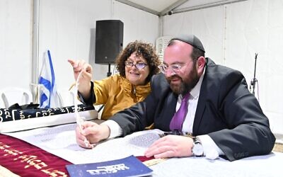 Michal David holds the tip of a quill as Rabbi David Avraham writes the initials of her five grandchildren in a Torah scroll in Tel Aviv, Israel on November 27, 2023. (Canaan Lidor/Times of Israel)