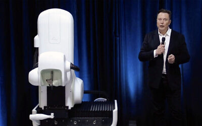 A video grab made from the online Neuralink livestream shows Elon Musk standing next to the surgical robot used to implant a device in the brain, seen during a Neuralink presentation on August 28, 2020. (Neuralink / AFP)