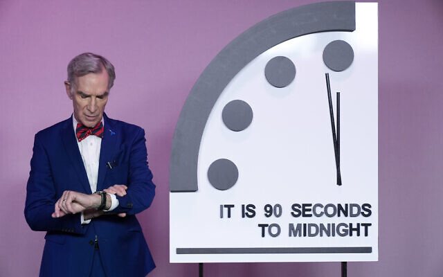 Science educator Bill Nye, looks at his watch next to the 'Doomsday Clock,' shortly before the Bulletin of the Atomic Scientists announces the latest decision on the 'Doomsday Clock' minute hand, Tuesday, Jan. 23, 2024, at the National Press Club Broadcast Center, in Washington, DC. (AP Photo/Jacquelyn Martin)