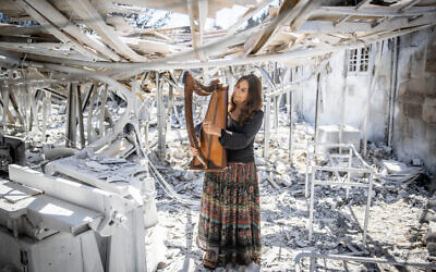 Shoshanna Harari plays a harp in the ruins of her harp-making factory after a forest fire, Moshav Ramat Raziel, near Jerusalem, August 18, 2021. (Yonatan Sindel/Flash90)