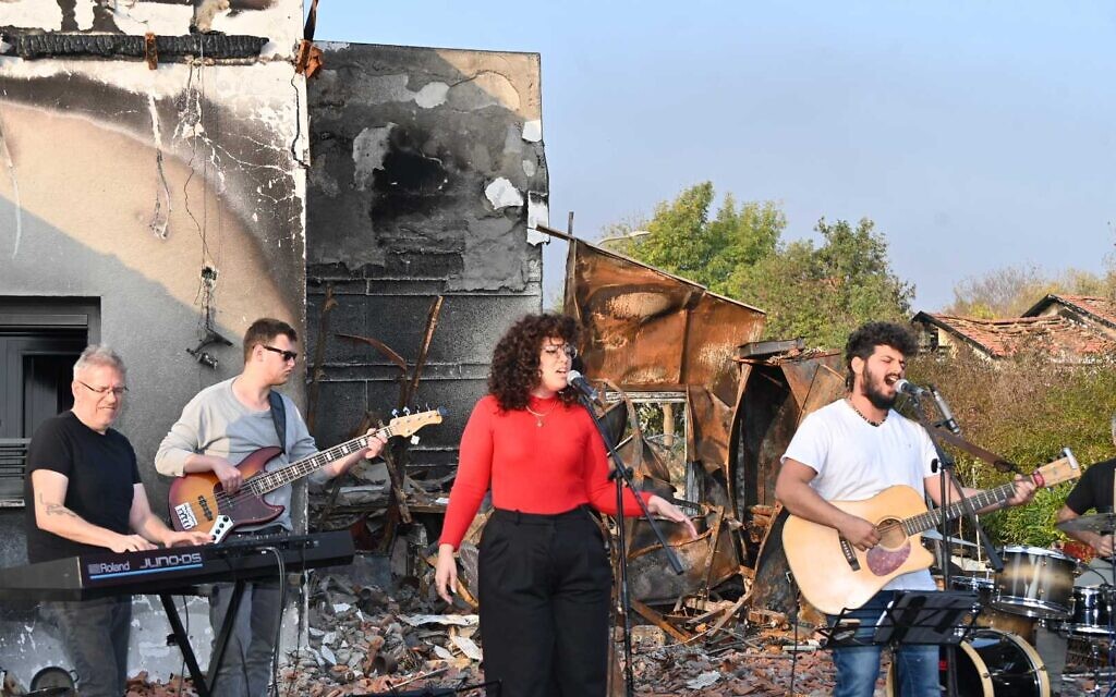Daniel Weiss, right, performs with a band on the charred remains of his parents' home in Be'eri on January 1, 2024. (Canaan Lidor/Times of Israel)