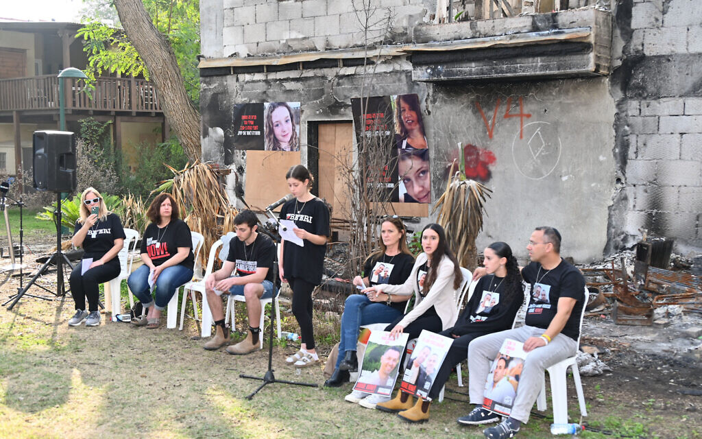 Released hostages and survivors speak to journalists in front of the charred remains of the home of Raaya and Hila Rotem in Be'eri on January 1, 2024. (Canaan Lidor/Times of Israel)