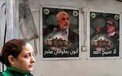 A woman walks past posters depicting Yahya Sinwar (L), the head of Hamas  in the Gaza Strip, and Abu Obeida (R), the masked spokesman of Hamas's Qassam Brigades, plastered on a wall in the Burj al-Barajneh camp for Palestinian refugees in Beirut's southern suburb on February 5, 2024. (ANWAR AMRO / AFP)