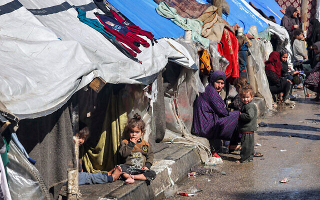 A woman and children sit outside tents sheltering displaced Palestinians in Rafah in the southern Gaza Strip on February 8, 2024. (Mohammed Abed/AFP)