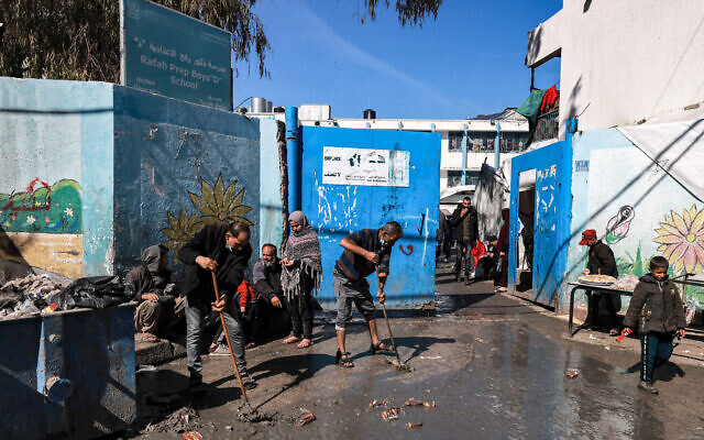 Men sweep water away from the entrance of a school run by UNRWA that is sheltering displaced Palestinians in Rafah in the southern Gaza Strip on February 8, 2024, amid the ongoing war between Israel and the Palestinian terror group Hamas. (Mohammed Abed/AFP)