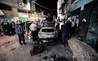 People inspect a burned car in an Israeli strike in the West Bank city of Jenin overnight on February 22, 2024. (Mohammad Mansour/AFP)