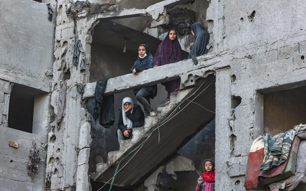 Palestinian women and children look on as they stand at the structure of a heavily damaged building on February 22, 2024, following overnight Israeli air strikes in Rafah in the southern Gaza Strip. (Mohammed Abed/AFP)