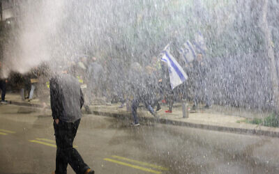 Protesters move away from a water jet used by security forces to disperse them during an anti-government demonstration in Tel Aviv on February 24, 2024 (JACK GUEZ / AFP)