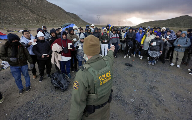 A Border Patrol agent asks asylum-seeking migrants to line up in a makeshift, mountainous campsite after the group crossed the border with Mexico, Friday, Feb. 2, 2024, near Jacumba Hot Springs, Calif. (AP Photo/Gregory Bull)