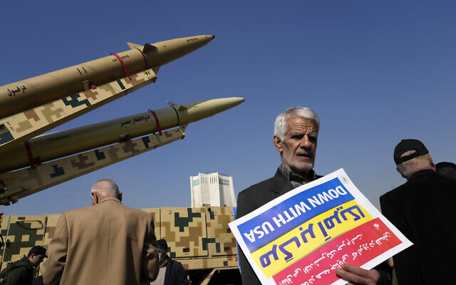 A man carries an anti-US placard upside down in front of the Iranian-made missiles displayed in the annual rally commemorating Iran's 1979 Islamic Revolution in Tehran, Iran, February 11, 2024. (Vahid Salemi/AP)