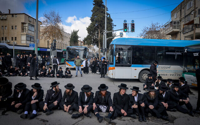 Haredi men block a Jerusalem road during a protest against the autopsy of a young boy who died, February 6, 2024 (Chaim Goldberg/Flash90)