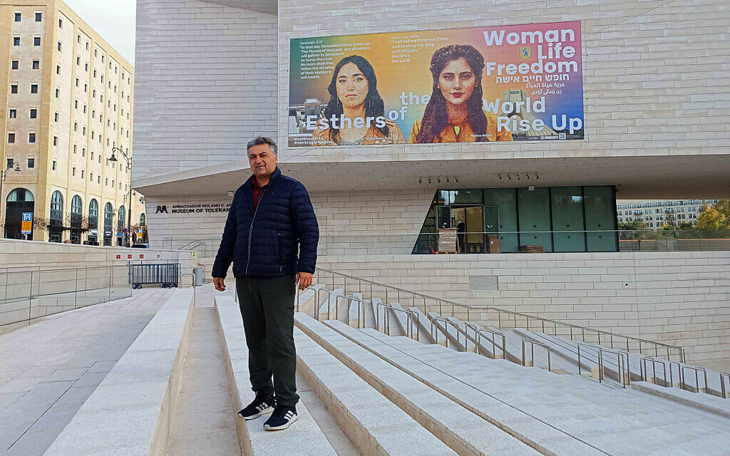 Iranian-American artist Hooman Khalili posing in front of a mural he designed on the outside wall of the Jerusalem Museum of Tolerance depicting slain Iranian-Israeli soldier Shirel Pour Haim (L) and Mahsa Amini, the woman who sparked protests in Iran after being killed by the regime, January 30, 2024 (Gianluca Pacchiani / Times of Israel)