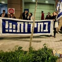 In a photo provided by anti-government activists, protesters hold a banner calling for elections outside the home of Intelligence Minister Gila Gamliel, in Tel Aviv, February 22, 2024. (Udi Salmanovich)