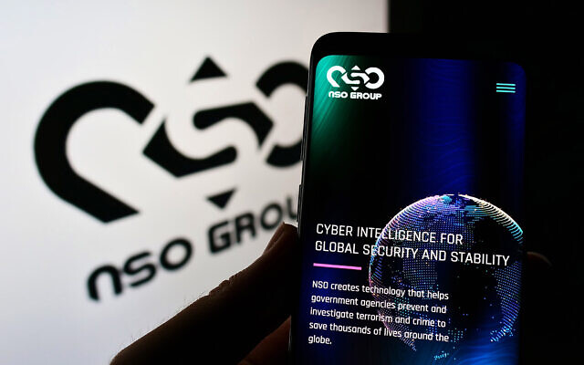 Illustrative: A person holding a smartphone showing the NSO Group Technologies website next to a screen with the company's logo (T. Schneider/Shutterstock.com)