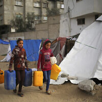 Palestinian girls carry water containers along a street in Rafah in the southern Gaza Strip on March 3, 2024. (AFP)