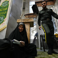 A woman fills out her ballot as a policeman walks past during the parliamentary and Assembly of Experts elections at a polling station in Tehran, Iran, Friday, March 1, 2024 (AP Photo/Vahid Salemi).