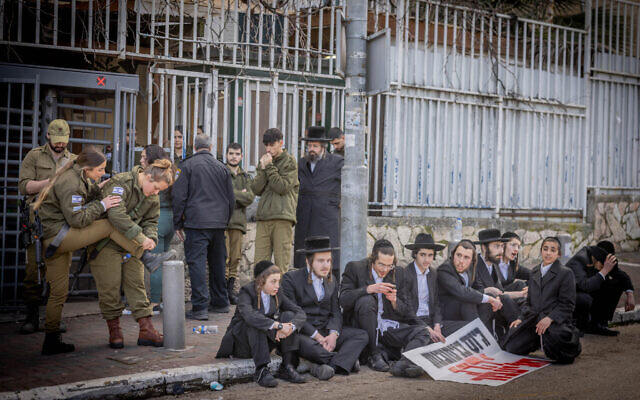 Ultra-Orthodox men after clashes during a protest outside the army recruitment office in Jerusalem, as a group of male and female soldiers stand behind them, March 4, 2024 (Chaim Goldberg/Flash90)