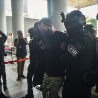 An Israeli man identified as Shalom Avitan (C) is escorted by Malaysian police upon his arrival at a court to face charges of possessing six handguns and 200 bullets in Kuala Lumpur on April 12, 2024. (Arif Kartono / AFP)