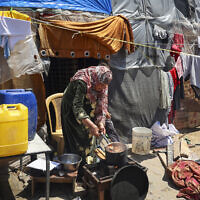 A woman cooks outside her makeshift shelter at a camp for displaced Palestinians in Rafah, in the southern Gaza Strip, on April 14, 2024 (AFP)