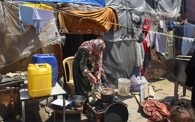 A woman cooks outside her makeshift shelter at a camp for displaced Palestinians in Rafah, in the southern Gaza Strip, on April 14, 2024 (AFP)