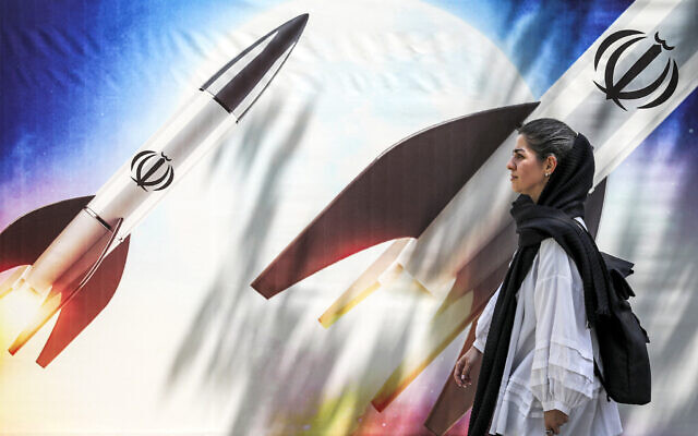 A woman walks past a banner depicting launching missiles bearing the emblem of the Islamic Republic of Iran in central Tehran on April 15, 2024. (ATTA KENARE / AFP)