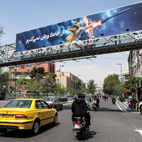A banner depicting the mythical Persian hero Arash the archer firing a missile from his bow, with text in Persian reading 'I will not abandon my homeland,' hangs on a suspended pedestrian bridge crossing in central Tehran on April 15, 2024. (Atta Kenare/AFP)