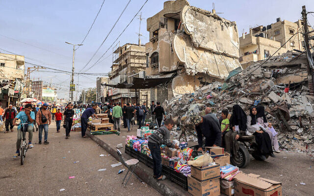 A boy helps a vendor arrange his merchandise as he sets up before the rubble of a collapsed building in Rafah in the southern Gaza Strip on April 23, 2024 (Photo by MOHAMMED ABED / AFP)