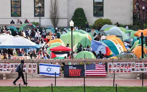 A man walks past Israeli and US flags alongside portraits of Israelis taken hostage by the Palestinian terror group Hamas, in front of the anti-Israel encampment at Columbia University in New York on April 23, 2024. (Charly Triballeau/AFP)
