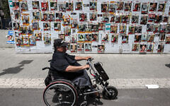 A person sitting in an electric wheelchair moves past posters of Israeli hostages held in Gaza by Hamas, in Tel Aviv on April 25, 2024. (Jack Guez/AFP)