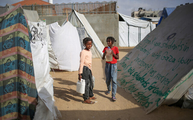 Children carry containers with water next to a tent bearing a message of thanks to students in the United States who have expressed solidarity with Gazans, at a camp for displaced Palestinians in Rafah, in the southern Gaza Strip on April 27, 2024. (AFP)