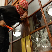 A demonstrator at Columbia University breaks the windows of the front door of the building in order to secure a chain around it to prevent authorities from entering as part of an anti-Israel demonstration, April 30, 2024. (Alex Kent/Getty Images/AFP)