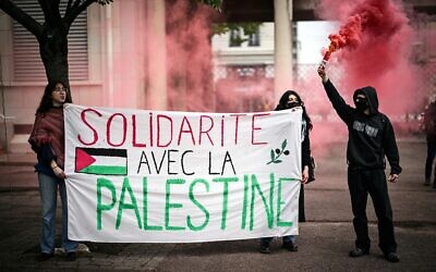 A demonstrator holds up flares as two others hold a banner reading in French 'Solidarity with Palestine' during a pro-Palestinian demonstration in the courtyard of the Institute of Political Studies (Sciences Po) building in Lyon, France, on April 30, 2024. (Olivier Chassignole/AFP)