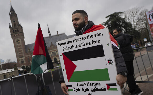 A pro-Palestinian, anti-Israel demonstrator holds a sign outside the International Court of Justice, rear, in The Hague, Netherlands, February 21, 2024. (AP Photo/ Peter Dejong)