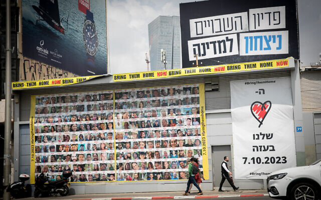 People walk by photographs of Israeli civilians held hostage by Hamas terrorists in Gaza,  in Tel Aviv. April 9, 2023. (Miriam Alster/FLASH90)