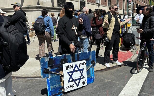 A masked protester near the Columbia University campus in New York City with a sign bearing a Star of David and the words 'Lie, Cheat, Steal, Kill,' April 24, 2024. (Cathryn J. Prince/Times of Israel)