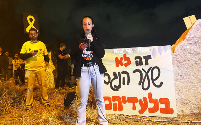 Lishai Miran, the wife of hostage Omri from Kibbutz Nahal Oz, speaks at a rally by returnees to the Sderot area at Sha'ar Hanegev Junction on April 6, 2024. The sign behind her reads: "It's not Sha'ar Hanegev without them." ( Tal Kamir)
